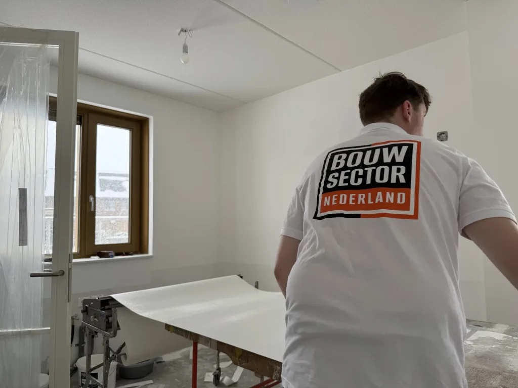 Behanger van Bouwsector Nederland rolt vlies af over de plaktafel naast een afgeplakte deur
