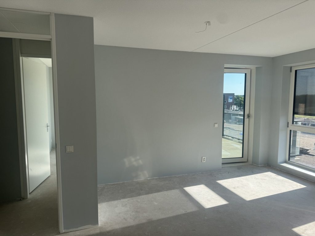 Lichtgrijze wanden in een nieuw appartement met betonvloer en balkondeur