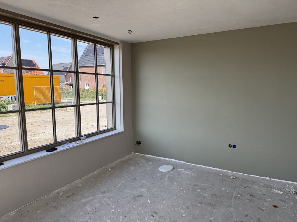 Kamer in een nieuwe woning met een groene wand en een groot raam met roeden