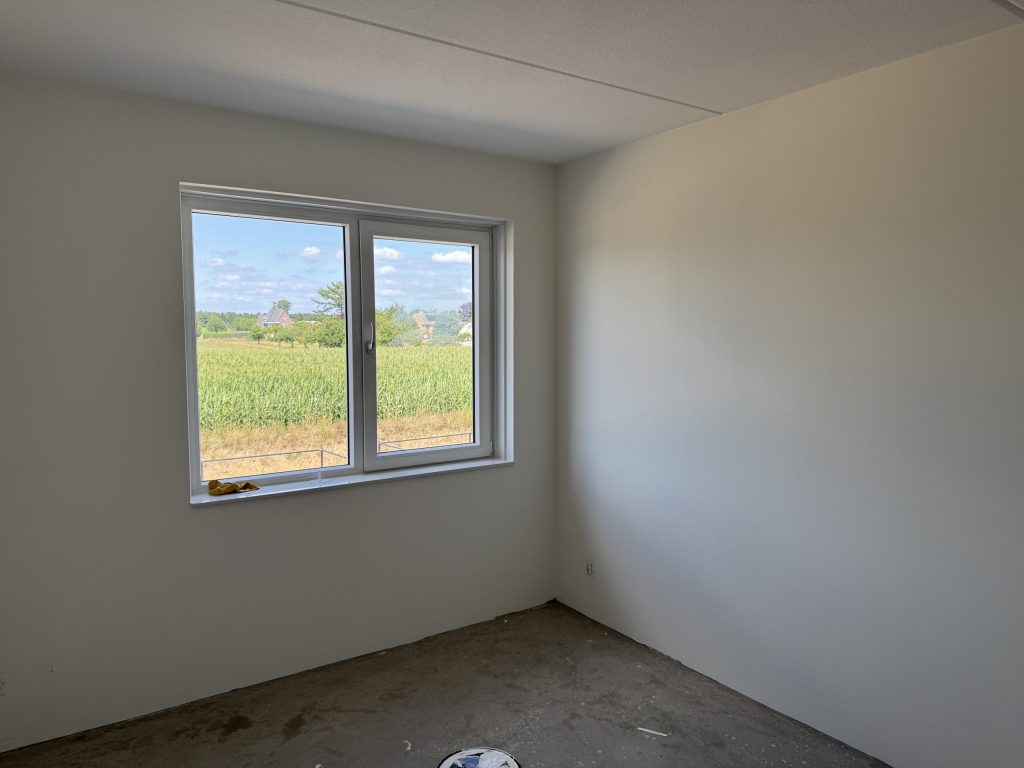 Lege slaapkamer met gladde lichte wanden en uitzicht over een maisveld