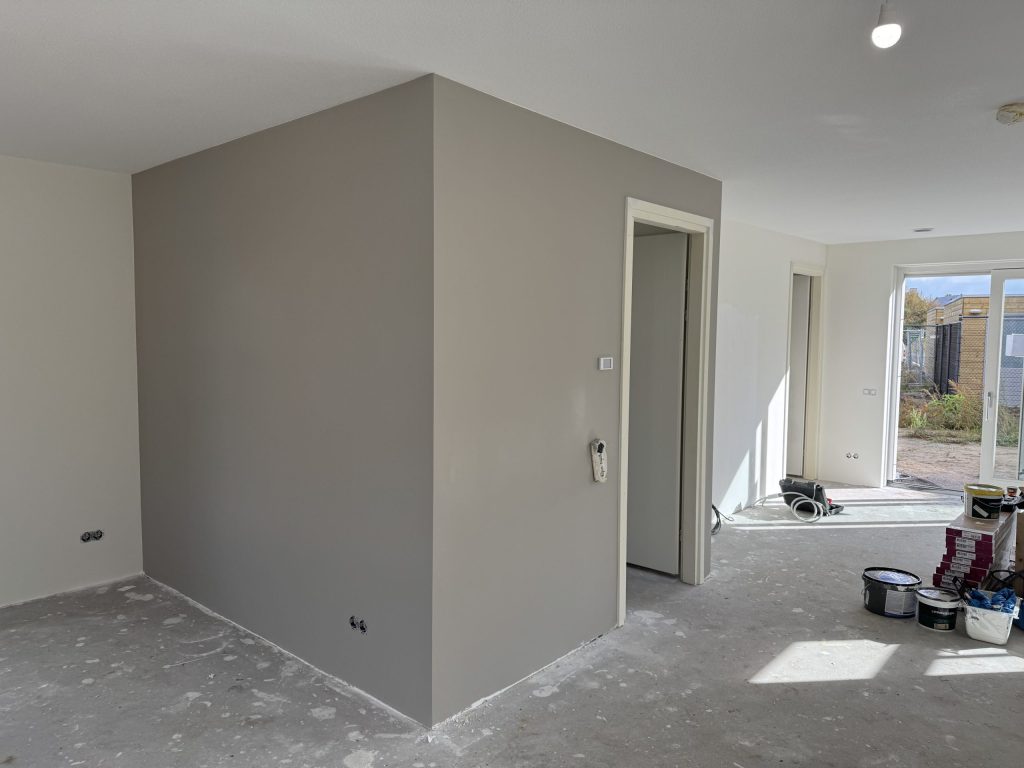 Woonruimte met een grijze wand rond de trapkast en emmers verf klaar voor de laatste laag