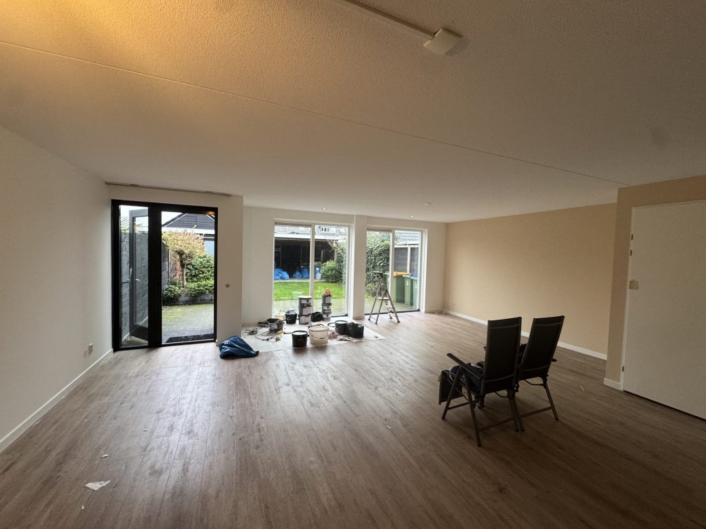 Leeggeruimde woonkamer met tuindeuren en verfemmers op de vloer, klaar voor de behanger
