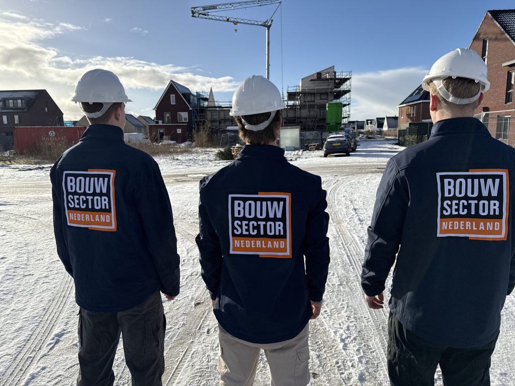 Drie vakmensen van Bouwsector Nederland met witte helm kijken naar huizen in aanbouw
