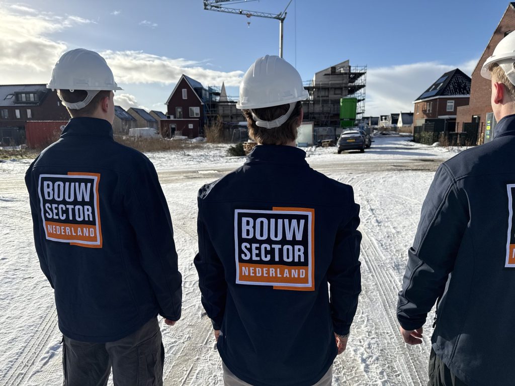 Vakmensen van Bouwsector Nederland met helm en logo op de jas bij een straat met nieuwbouw